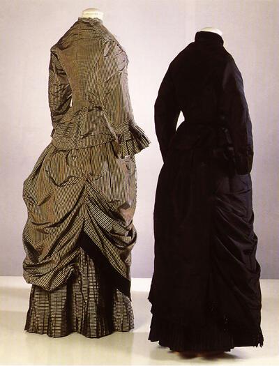 Twee damesensembles met tournure, benadrukt door de gedrapeerde overrok,1875, mode